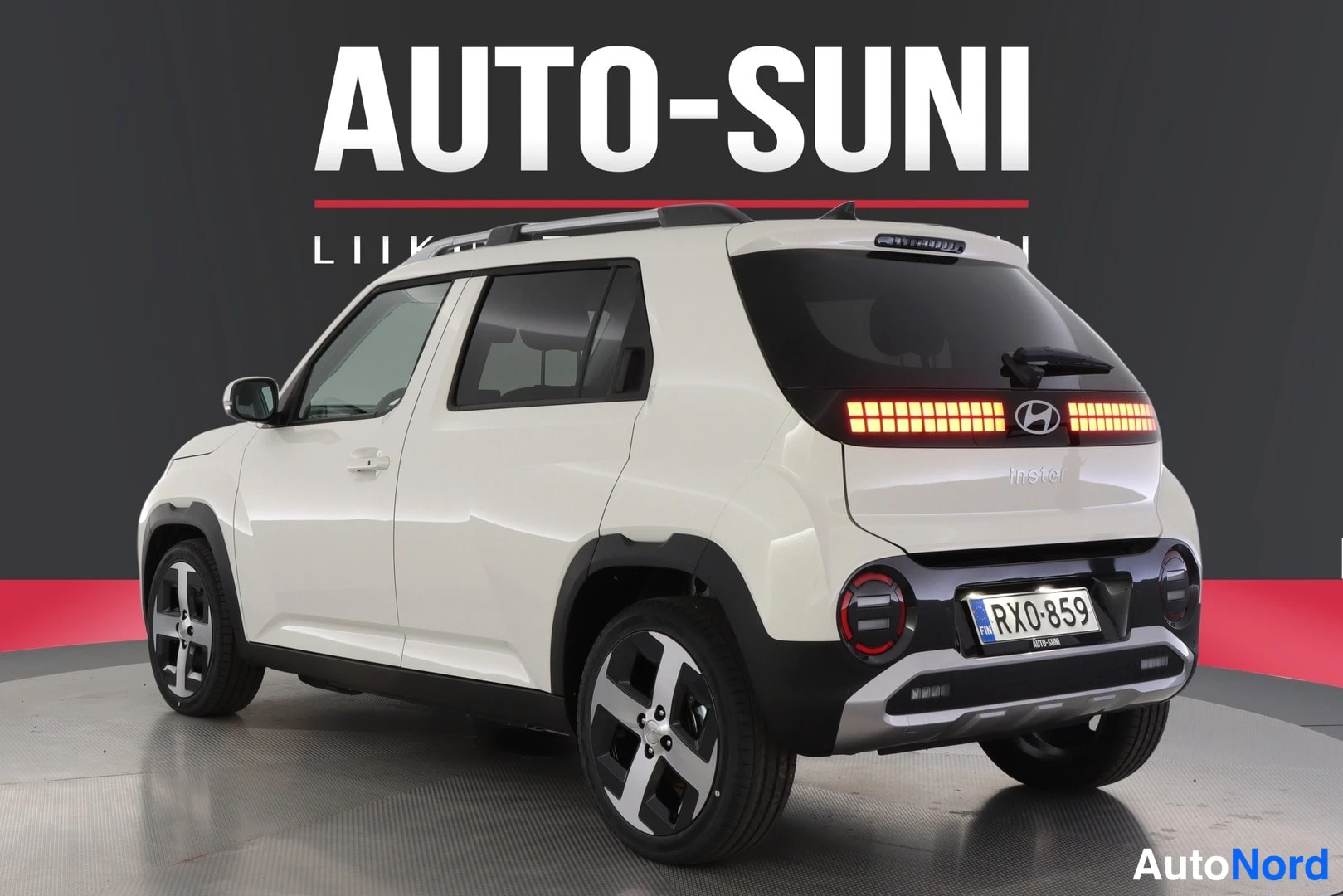 Takaviisto: Rear three-quarter view of the white car from the left side. The rear LED strip and lower taillights are lit up. Features such as roof rails, alloy wheels, and