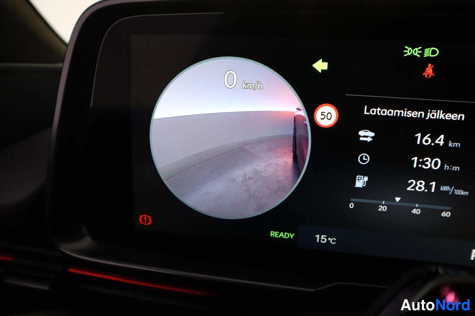 Edestä: Kojelaudan näyttö: pyöreä kamerakuva, nopeus 0 km/h, 'Lataamisen jälkeen' -tiedot 16,4 km, 1:30 h:m ja 28,1 kWh/100 km, 50-merkki, READY-merkki ja 15 °C.