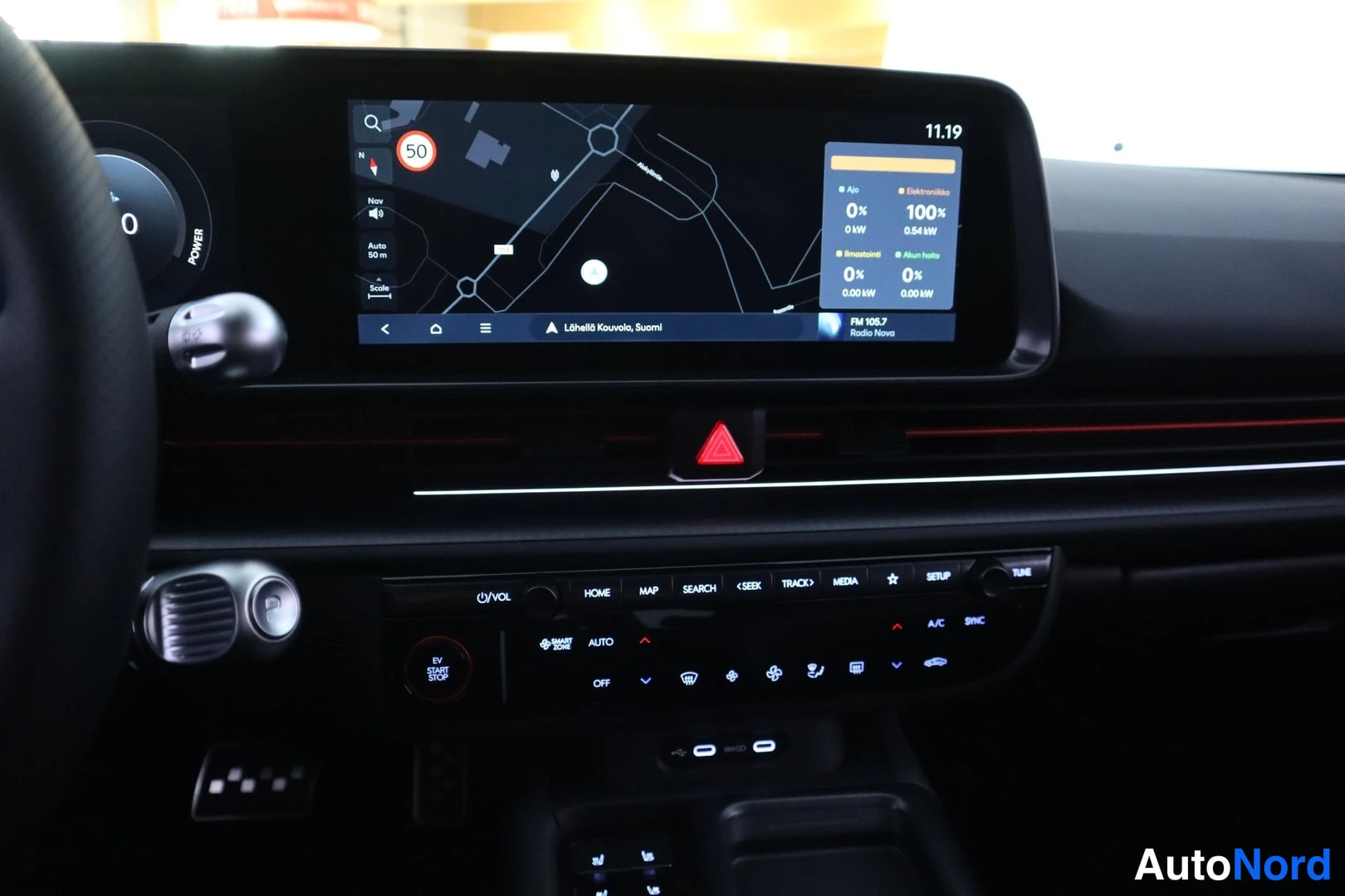 Edestä: Keskikonsoli: infotainment-näyttö navigointikartalla, hälytyskolmio, ilmastointipaneelin painikkeet (AUTO, A/C, SYNC, OFF), EV START STOP -painike sekä HOME-, M