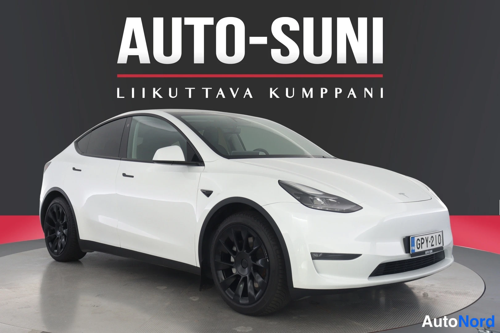Etuviisto, nokka oikealle: Valkoinen Tesla Model Y etuokoliskuvassa oikealta; mustat kevytmetallivanteet ja rekisterikilpi näkyvissä.
