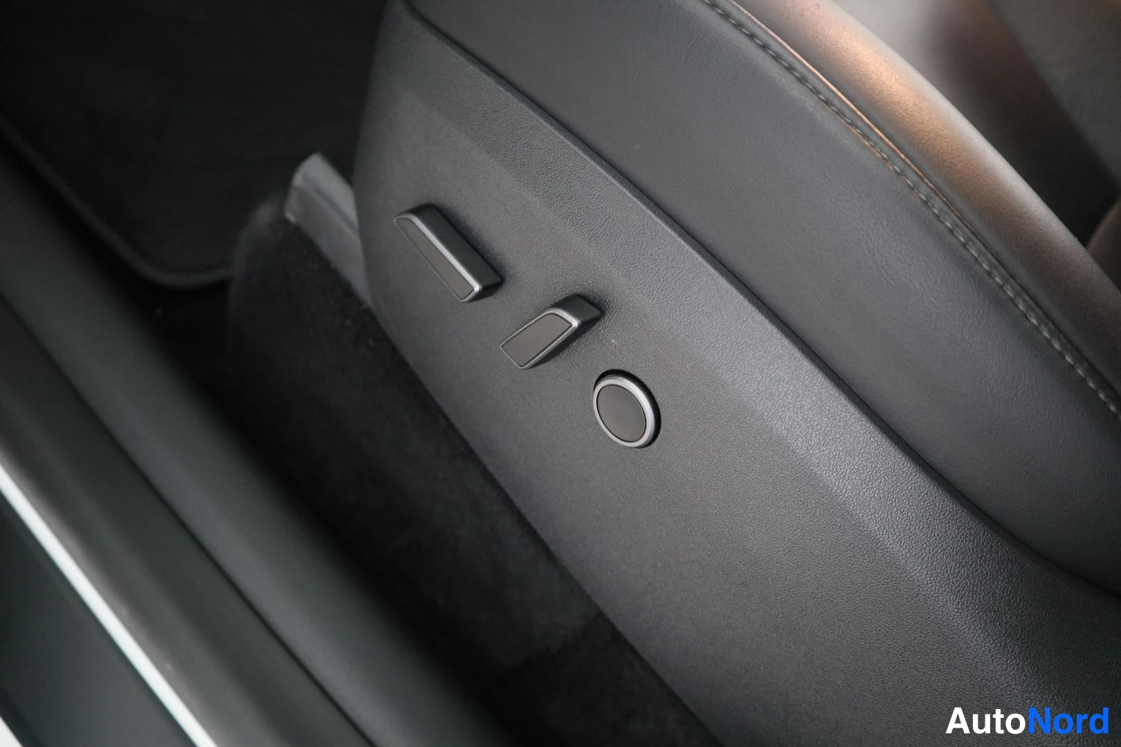 Yksityiskohta: Close-up of black seat with electrical adjustment levers and circular button