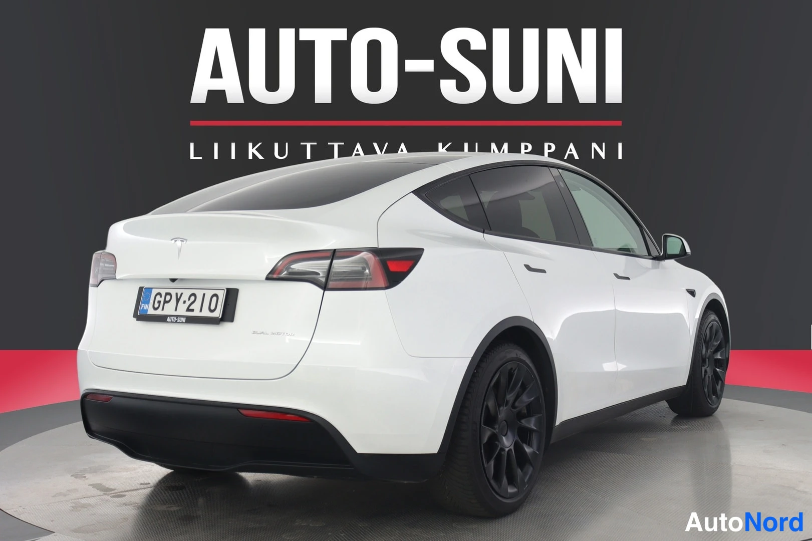 Takaviisto: Valkoinen Tesla Model Y kuvattuna suoraan takaa sivulta katsottuna; rekisterikilpi ja mustat vanteet.