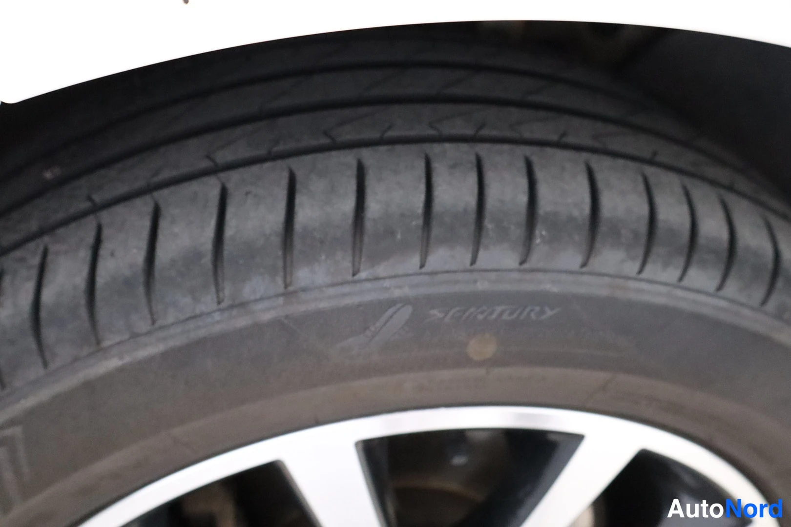 Yksityiskohta: Close-up of a black tyre with V-shaped tread blocks and the brand name 'SEVENTY' embossed on the sidewall. Part of a silver multi-spoke alloy wheel is visible.