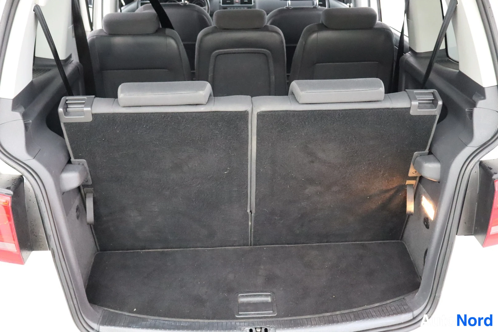 Tavaratila: Rear view through the open boot door showing the third-row seatbacks folded upwards. The seatback fabric is dark grey and has headrests attached at the top.