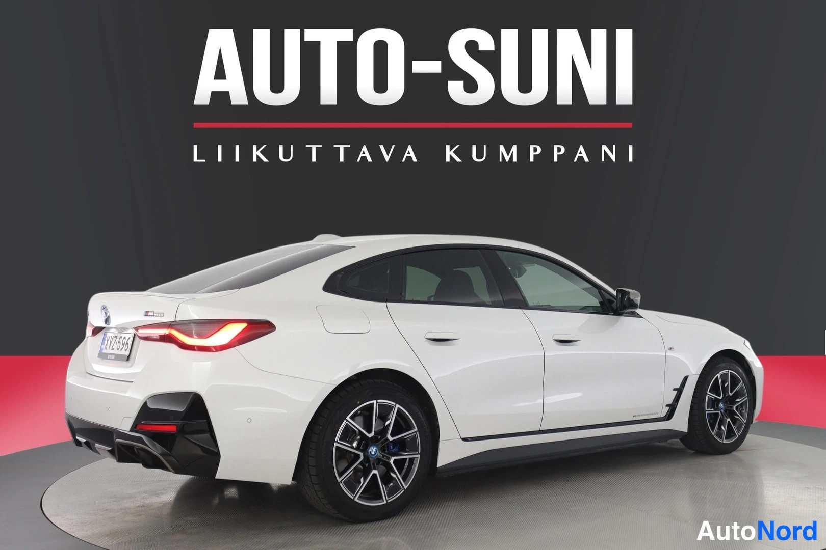 Takaviisto: Valkoinen BMW i4 Gran Coupé takaviistosta, perä kuvan vasemmalla; takavalot ovat valaistuneet punaisina ja musta takadiffuuseri näkyy, rekisterikilpi.