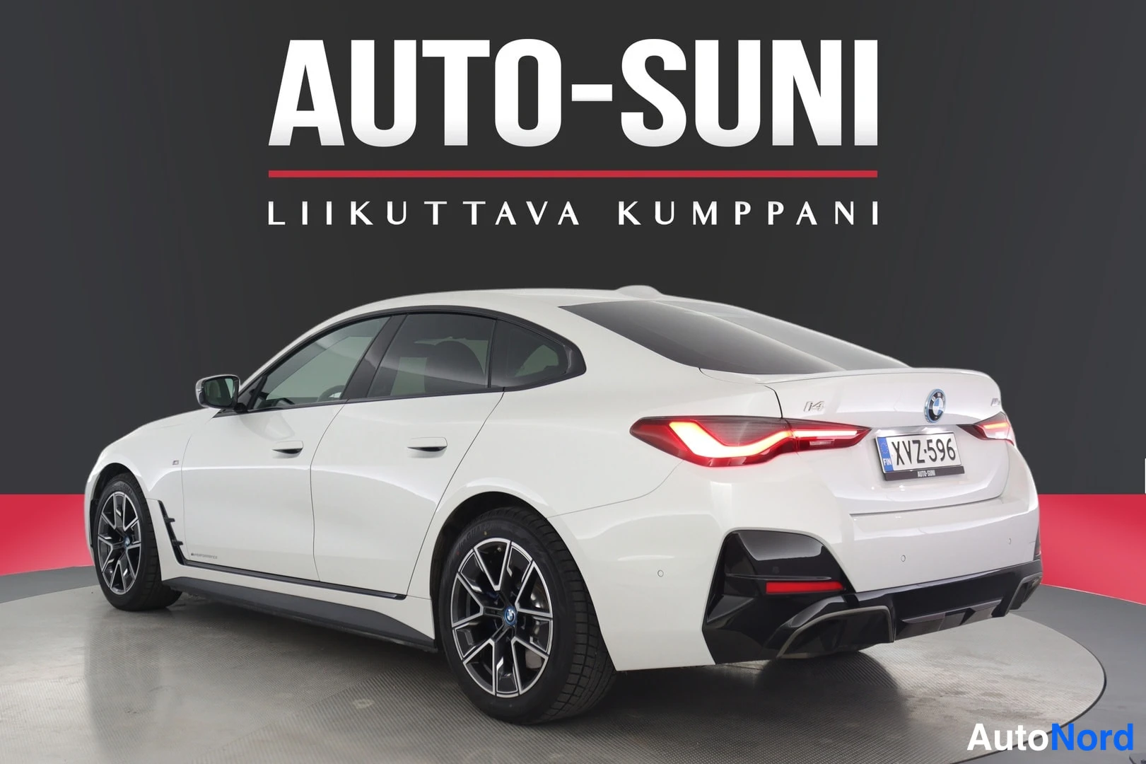 Takaviisto: Valkoinen BMW i4 takaviistosta, perä kuvan oikealla; takaluukussa i4-merkintä, oikea takavalo syttyneenä ja musta takadiffuuseri näkyy, rekisterikilpi.