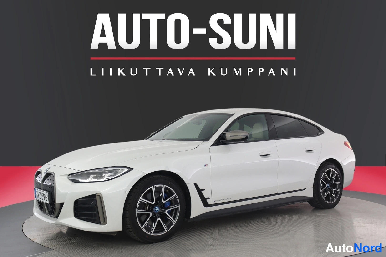Etuviisto, nokka vasemmalle: Valkoinen henkilöauto etu-nurkkakulmasta vasemmalta kuvattuna studiotaustaa vasten; etusäleikkö, ajovalot ja kylki näkyvät, yläosassa AUTO-SUNI-kyltti.