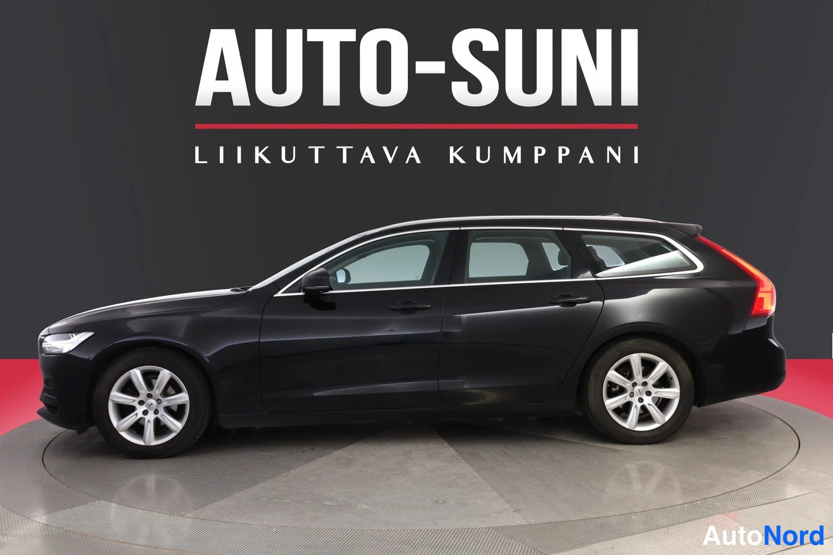 Etuviisto, nokka vasemmalle: Auton sivukulman näyttävä kuva tumman musta farmariauto valmetallilla, edessä AUTO-SUNI-mainoskyltti.