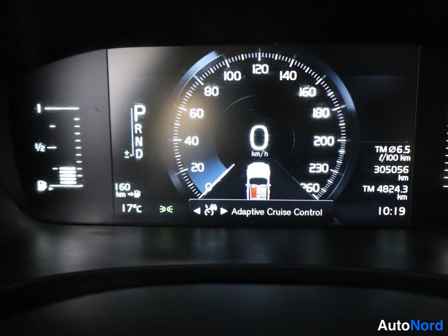 Yksityiskohta: Mittaristön näyttö: nopeus 0 km/h, vaihde P, kirjattu matka 305056 km, huoltomatka 4824,3 km, Adaptive Cruise Control aktiivinen.