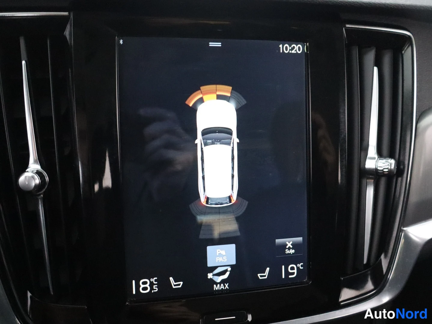 Ohjaamo: Vertical central infotainment screen displaying a 3D top-down graphical view of a white car with orange arc indicators around it, likely showing parking assist