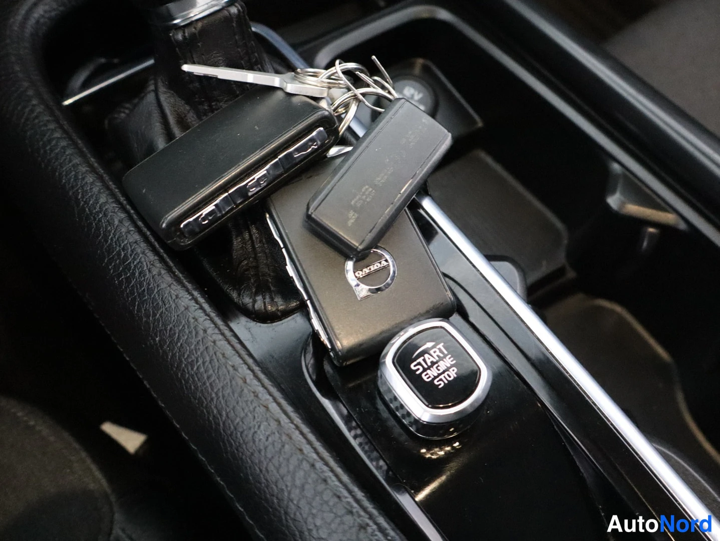 Yksityiskohta: Detail shot of the centre console gear selector area showing ignition keys on top and a START ENGINE STOP button.
