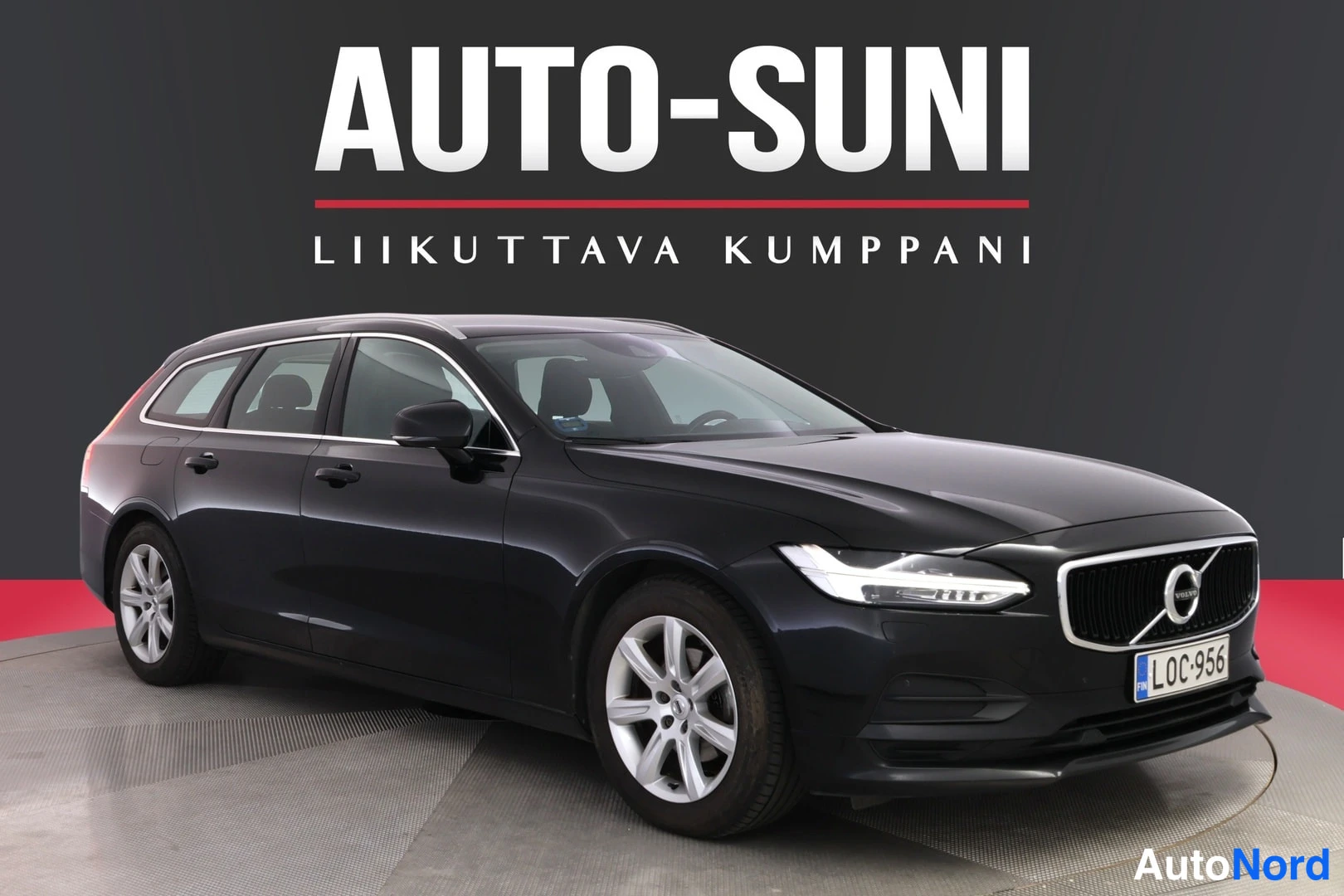 Etuviisto, nokka oikealle: Musta farmariauto Auto-Suni-logoa vasten, kolmasosan etukuva nokka oikealla.