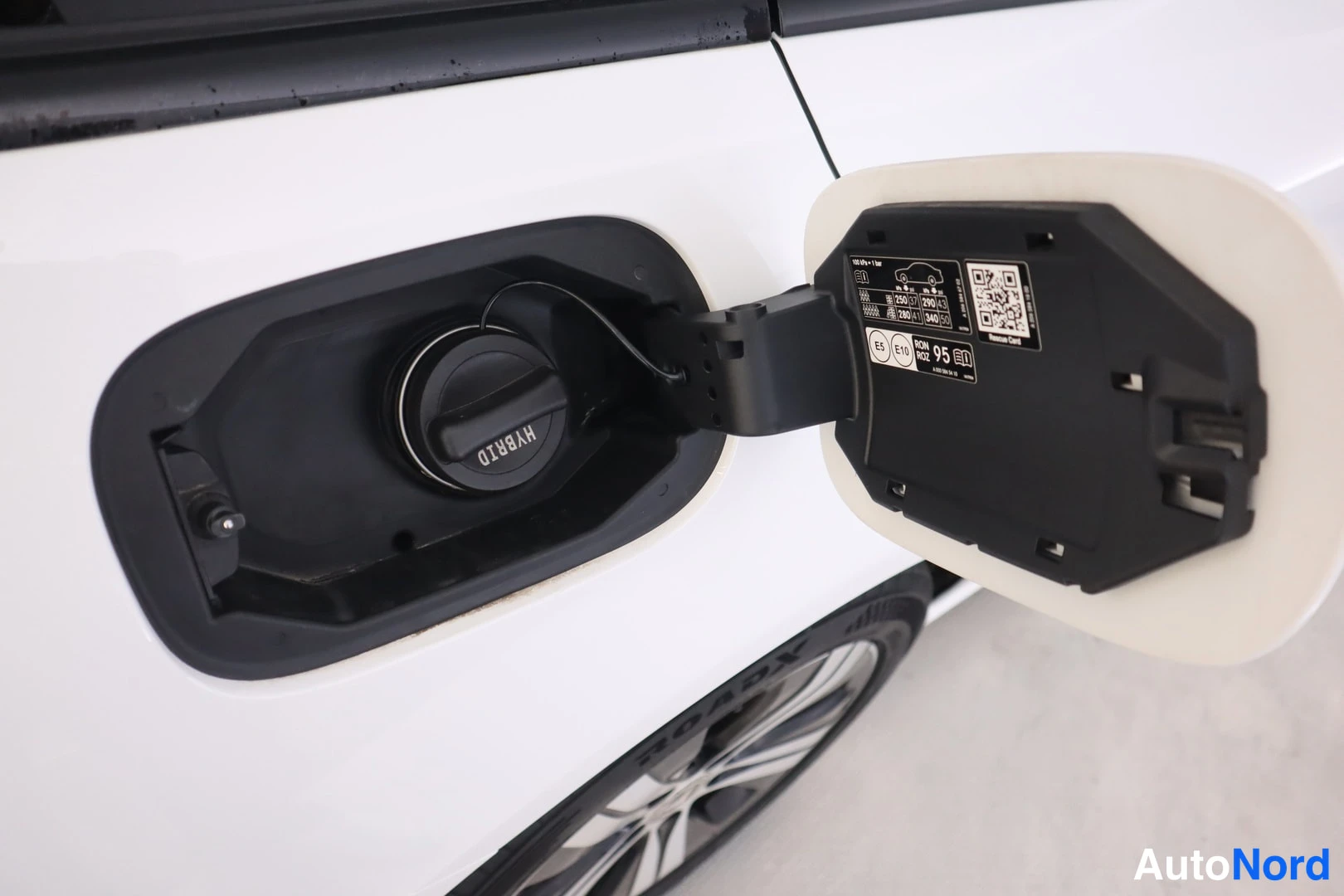 Sivulta: Auki avattu polttoainetäyttöaukko valkoisessa autossa;mustassa tankissa lukee HYBRID ja kannessa on merkintäkon 95 E10.
