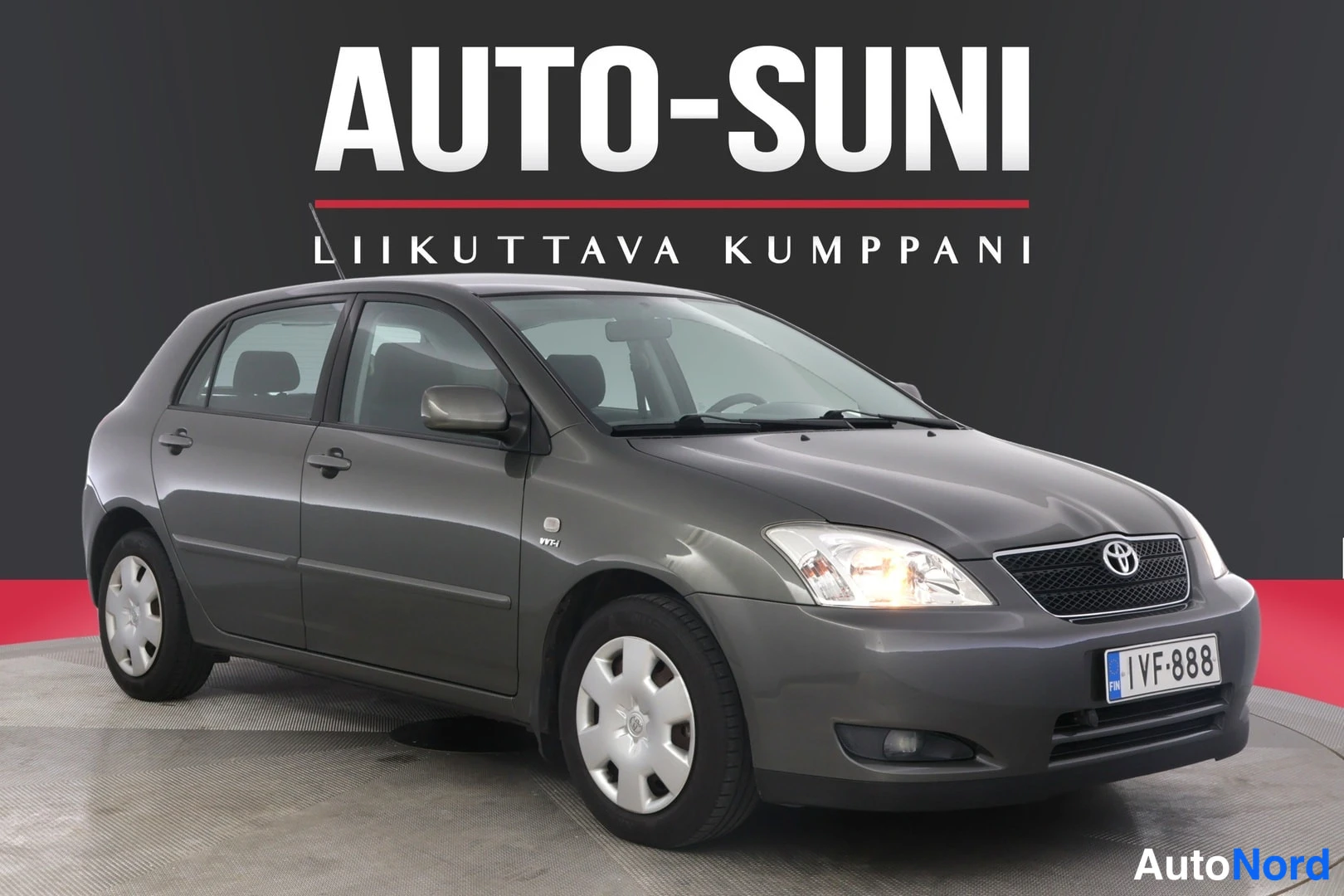 Etuviisto, nokka oikealle: Kuvassa harmaanharmaa Toyota Corolla -auton etu- ja vasen sivu. Etusäleikkö, Toyota-logo ja rekisterikilpi näkyvät. Valot ovat päällä.
