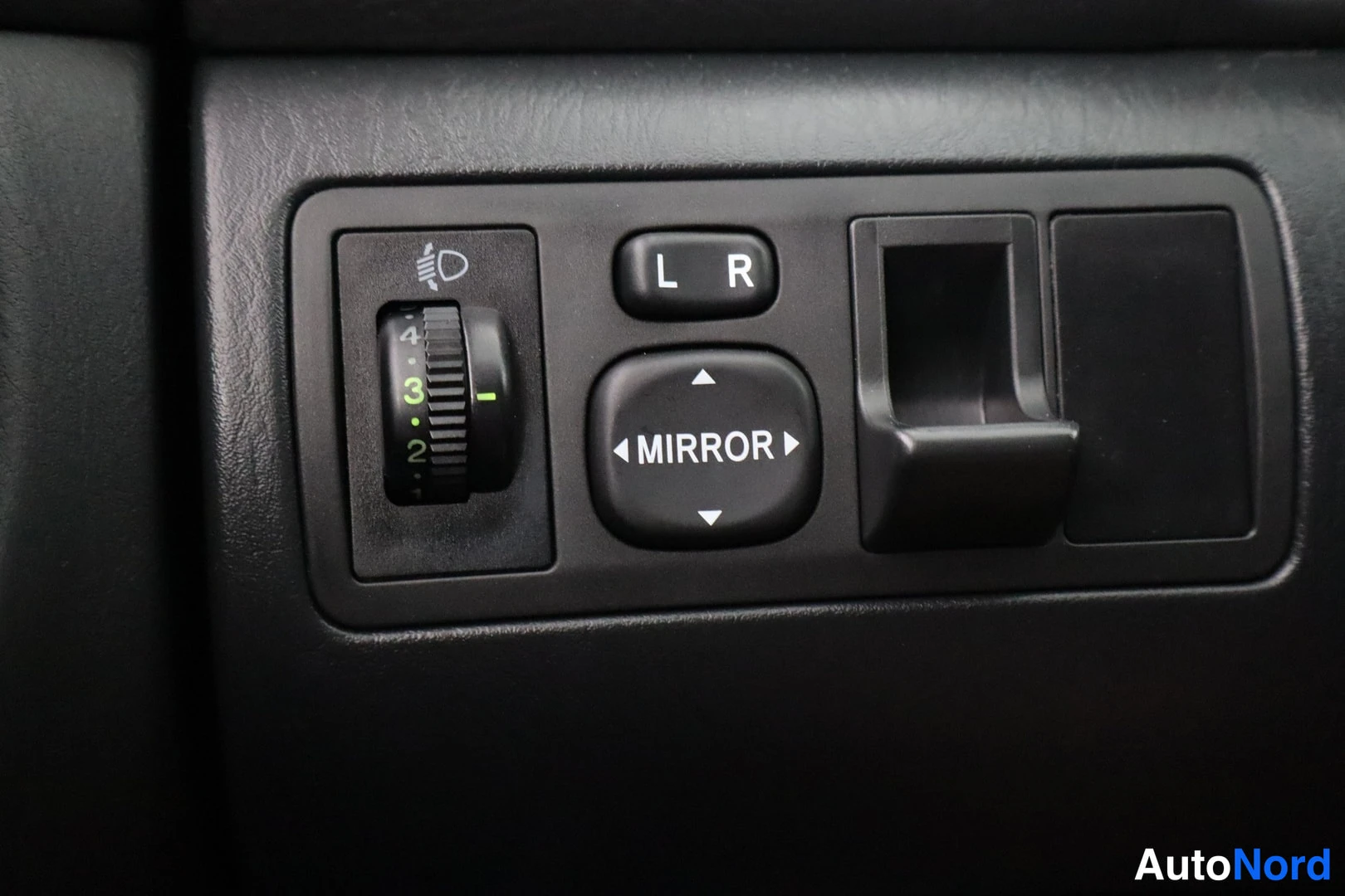 Yksityiskohta: Panel of black controls including a light switch and manual adjustment buttons for side mirrors with L R MIRROR labels.