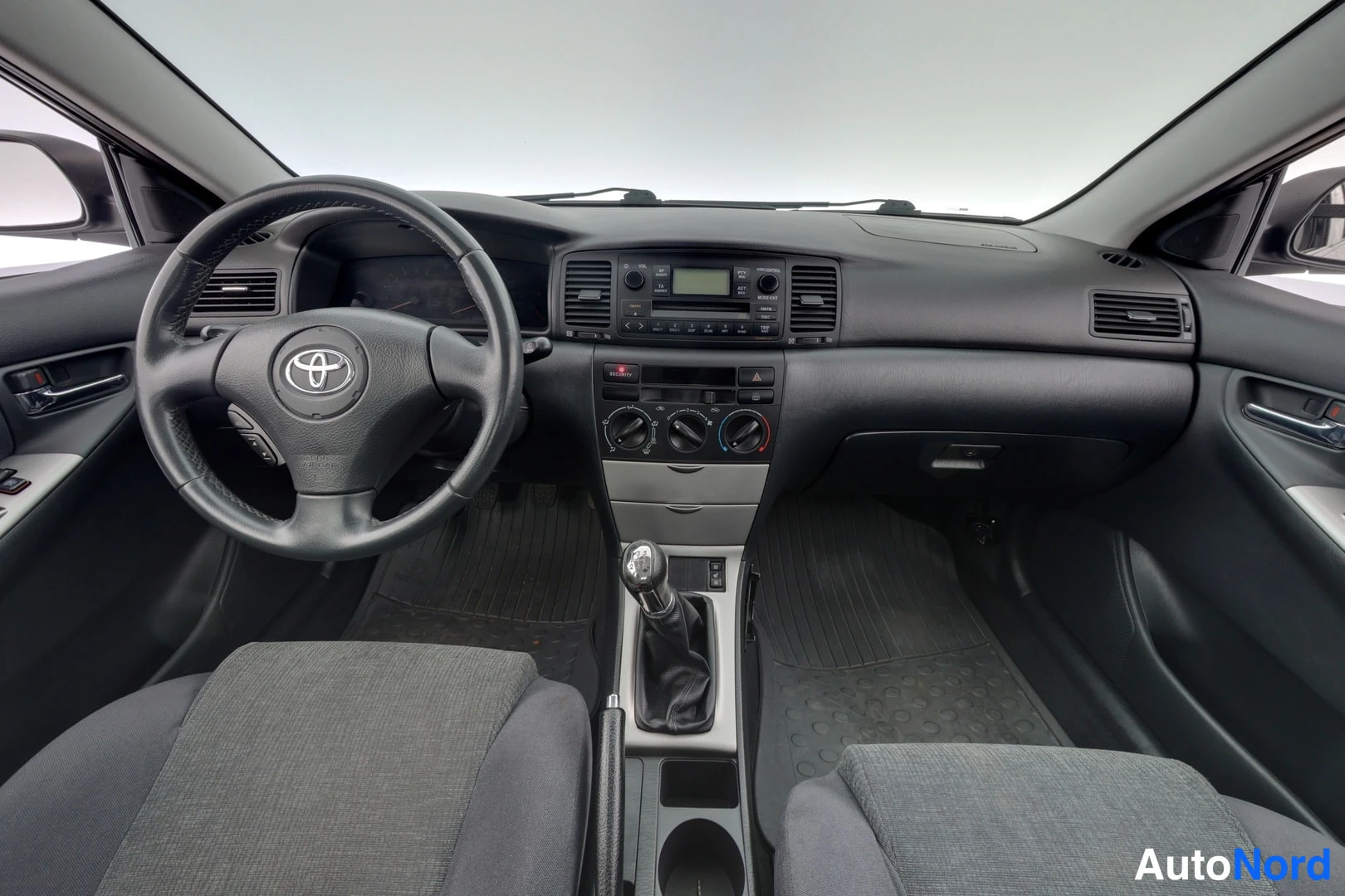 Muu: Ohjaamo harmaasta sisustasta: Toyota-ohjauspyörä, manuaalivaihteen vaihdekeppi, radiopaneeli ja kaksi etuistuinta.