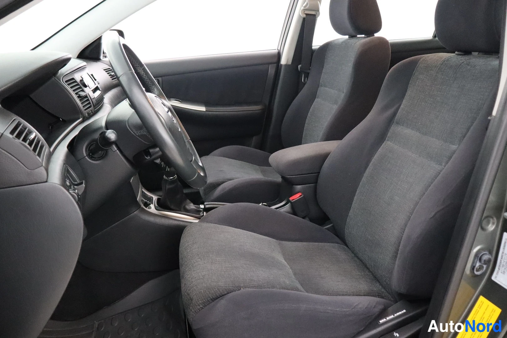 Etuistuimet: Interior shot showing black fabric front and rear seats, steering wheel with gear shifter in center console.