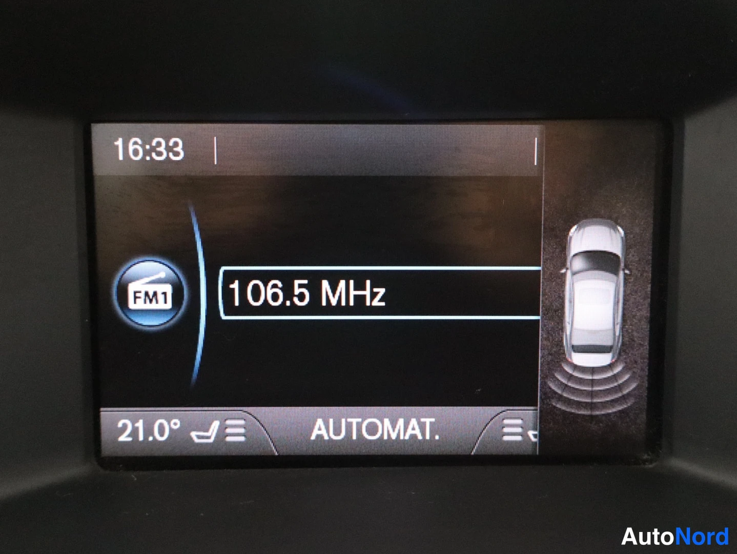 Yksityiskohta: Infonäyttö radionäytöllä FM1 106.5 MHz ja oikealla auton kuvituskuva pysäköintitunnistimen aalloilla.