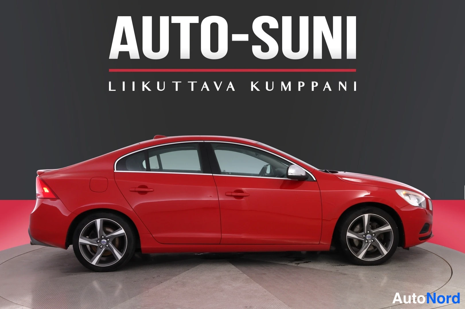 Etuviisto, nokka oikealle: Punainen Volvo S60 -sedan sivulta etuosaa kohti kuvattuna, liiketilan musta-punainen tausta ja Auto-Suni-logo.
