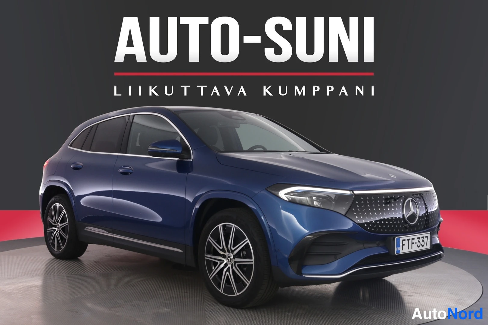 Etuviisto, nokka oikealle: Sininen Mercedes-Benz EQA -maastauto etukulmasta autonäyttelylavalla, rekisterikilpi.