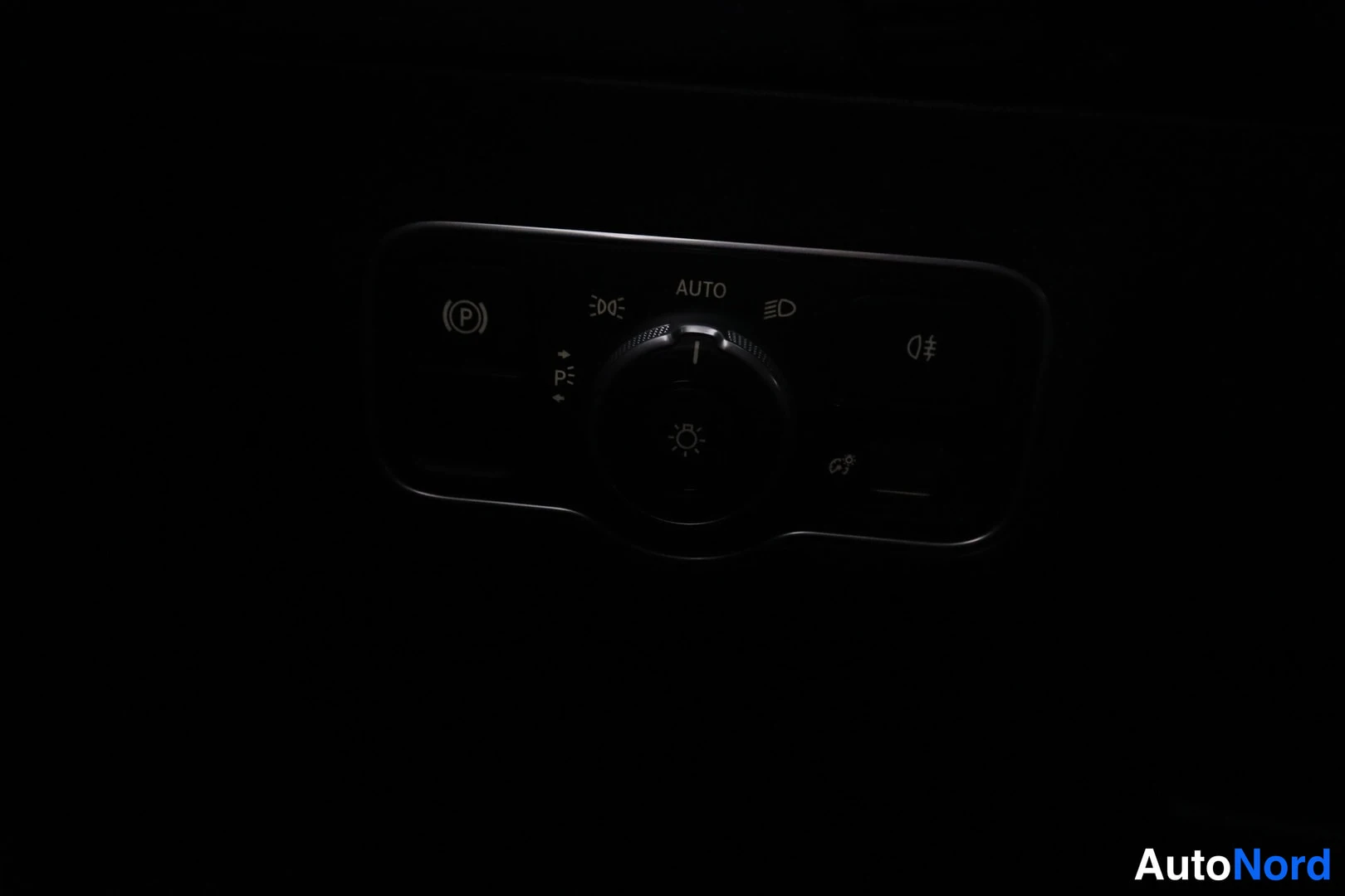 Yksityiskohta: Valokytkimen paneeli AUTO-merkinnällä, sumuvalojen symboleilla ja sähköisen seisontajarrun (P)-napilla; kuva on hyvin pimeä.