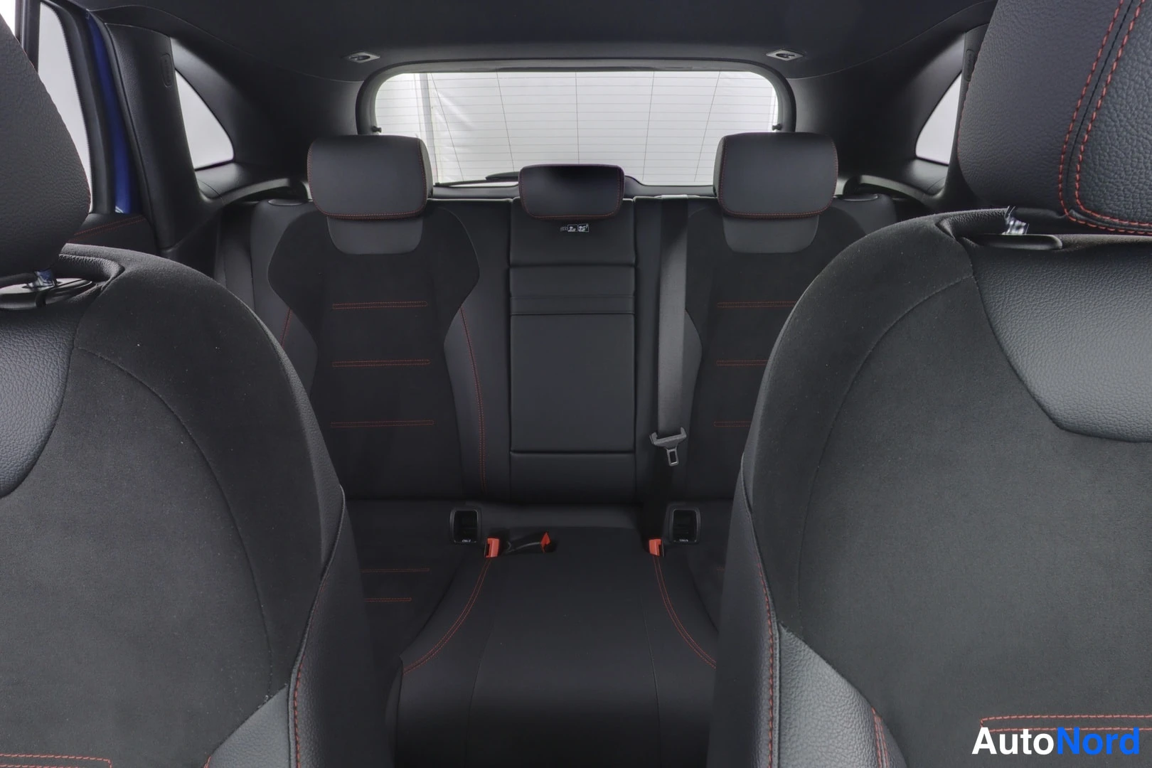Takaistuimet: Rear passenger area featuring black seats with red contrast stitching and three headrests visible. Rear window defroster lines are present on the rear glass.