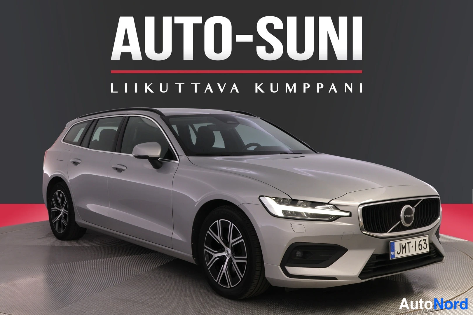 Etuviisto, nokka oikealle: Auton keula ja vasen sivu kuvassa oikealta; hopeanharmaa farmariauto, rekisteri.