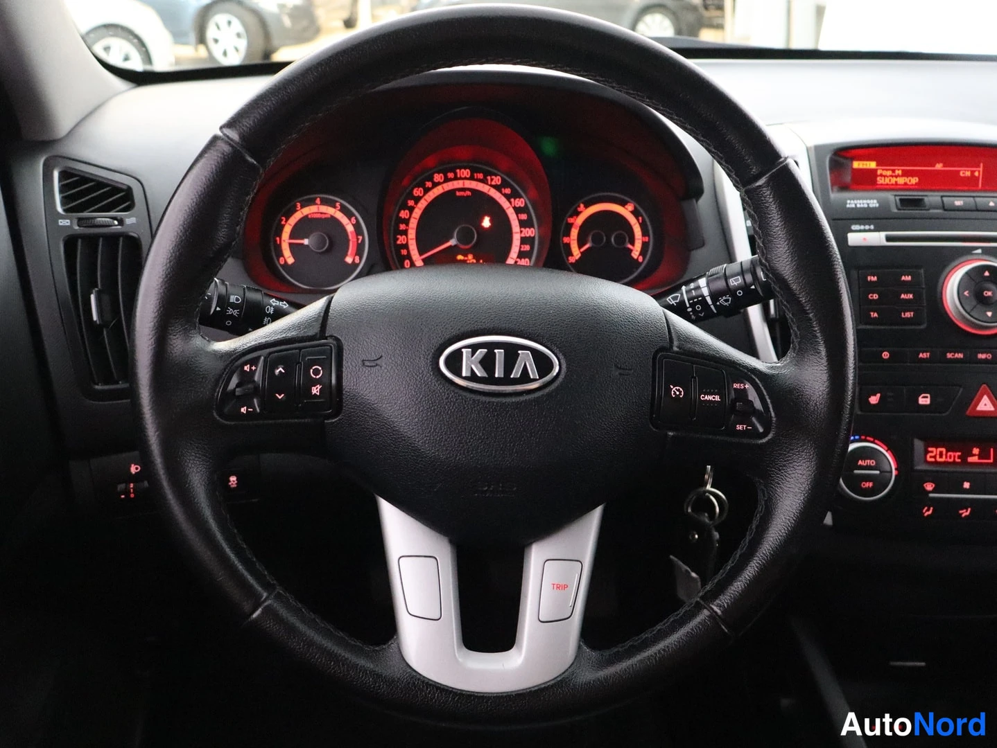 Muu: Kia-merkkisen auton ohjauspyörä ja kojelauta, nappien tekstejä RES+, SET-, CANCEL, radion näytössä SUOMIPOP ja lämmitin 20,0 °C.