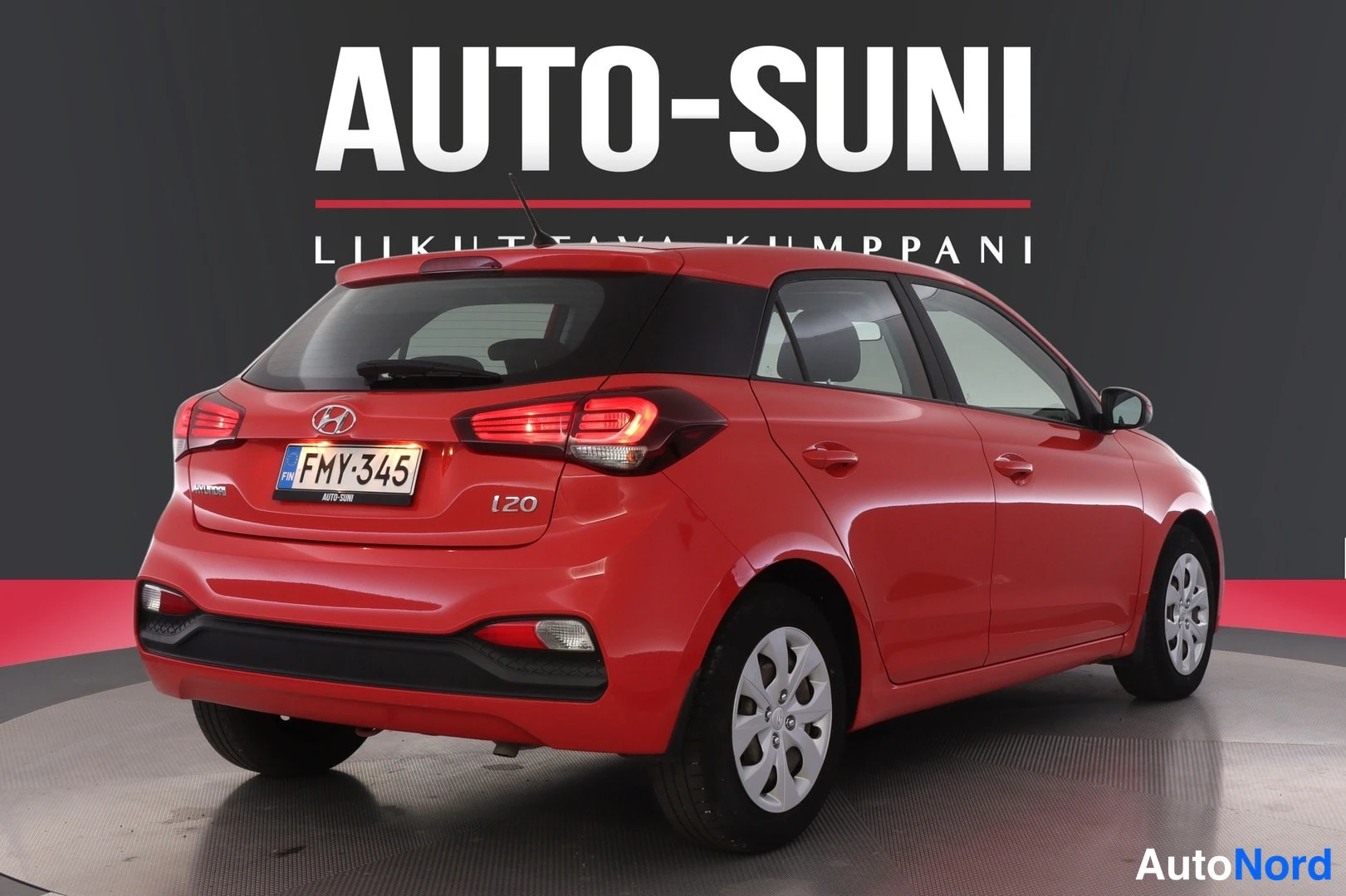 Takaviisto: Punaisen Hyundai i20:n takakulmakuva, takaluukussa rekisteritunnus ja i20-merkintä, kolme lohkolamppua näkyvissä.