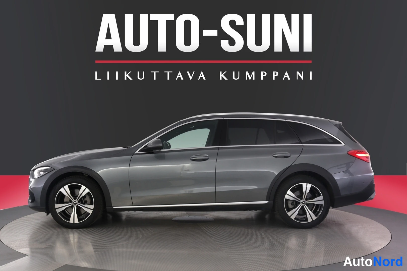 Sivulta: Auton sivukuva: harmaa Mercedes-Benz farmari, koko ajoneuvo näkyy kuvassa.