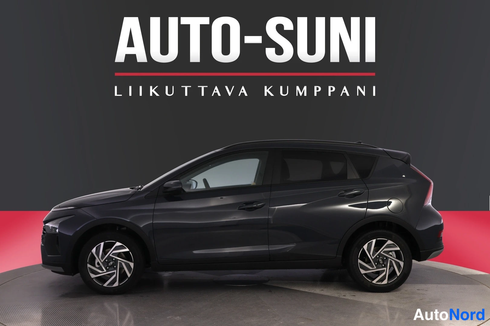Sivulta: Hyundai Bayon -farmarityylisen hatchbackin sivukuva vasemmasta sivusta, autossa tummat koripaneelit ja kevytmetallivanteet studio­taustaa vasten.