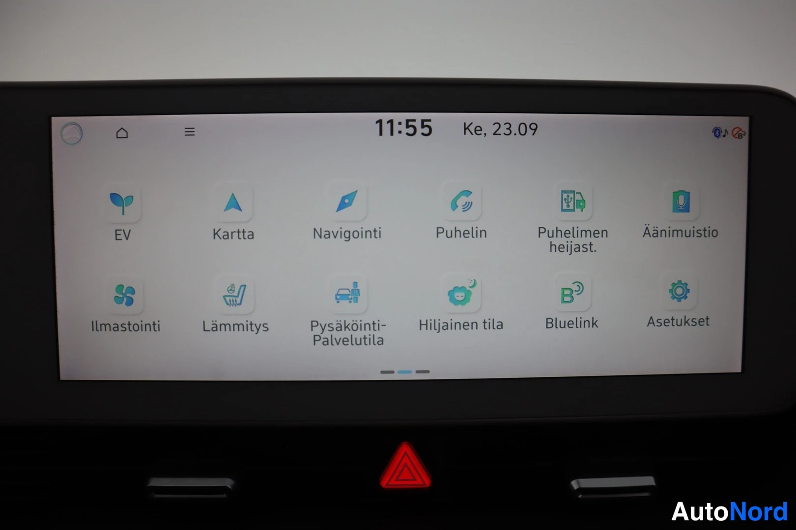 Yksityiskohta: Auton infotainment-näytön päävalikko: EV, Kartta, Navigointi, Puhelin, Ilmastointi, Lämmitys, Bluelink ja Asetukset -kuvakkeet.
