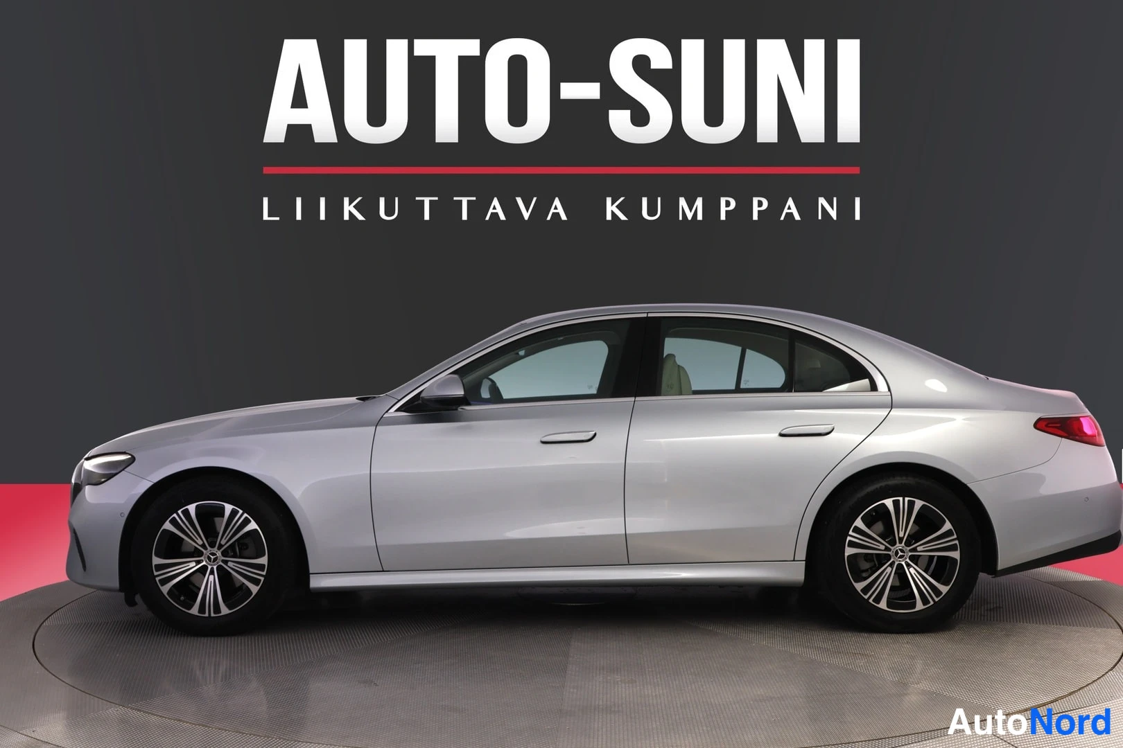 Sivulta: Auton sivuprofiili: hopeanharmaa sedan koristelevaa myyntihallia tummaa taustaa vasten.