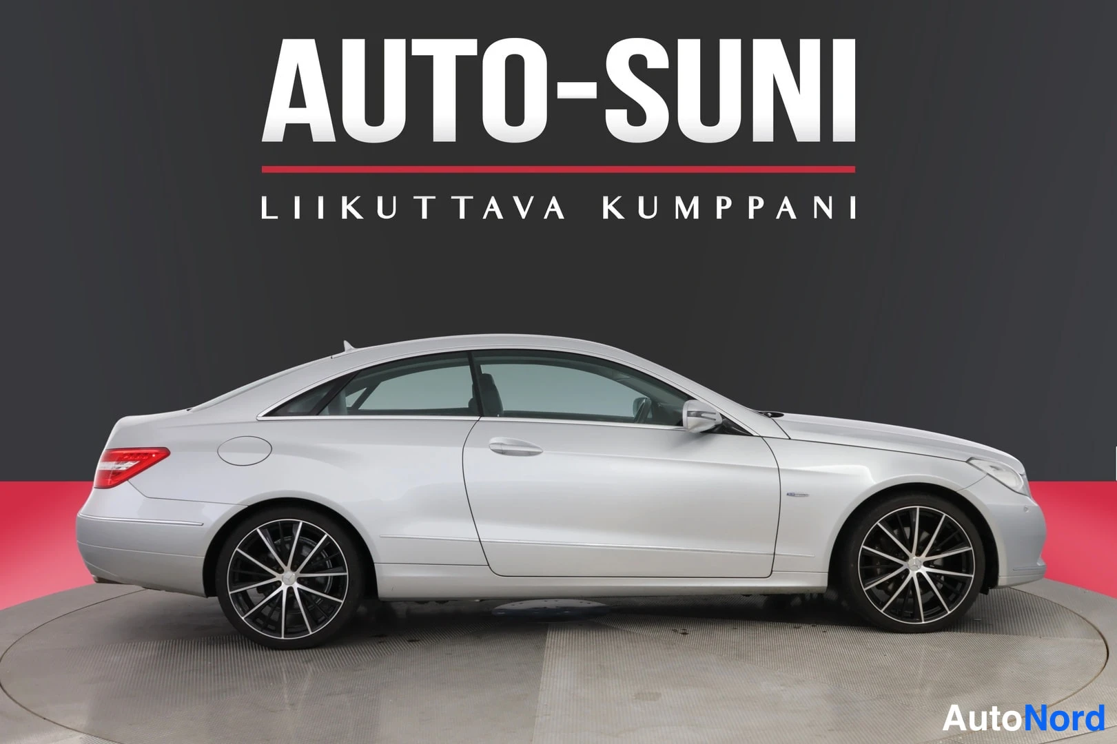 Sivulta: Mercedes-Benz-coupén sivukuva, hopeanvalkoinen koritys, kattolinja ja oven linjat, mustat monipuoliset vanteet, kuvan yläosassa AUTO-SUNI-logo.