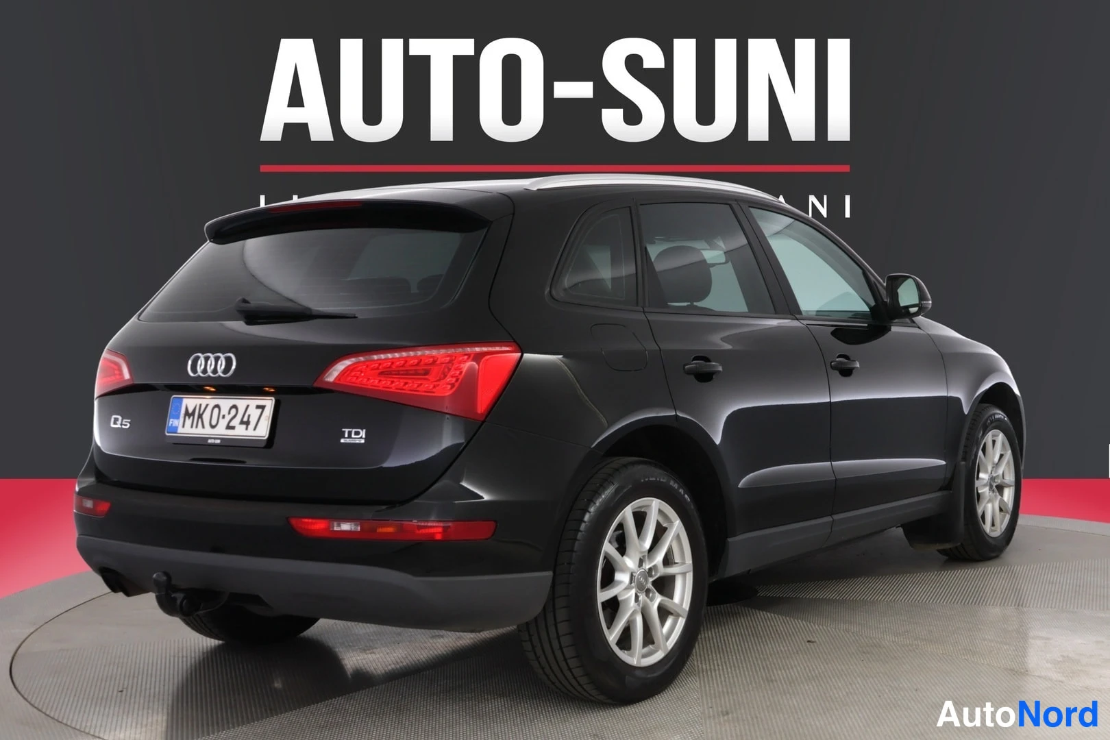 Takaviisto: Mustan Audi Q5:n takakulmanäkyvä sivukuva, rekisterikilpi, taustalla tumma seinä.
