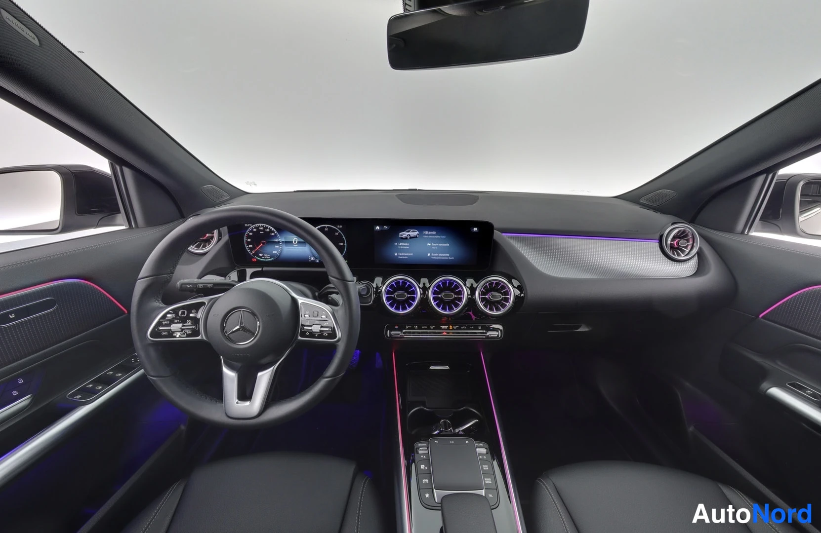 Muu: Mercedes-Benz EQA:n ohjaamo kuvattuna takaistuimelta: kaksiosainen näyttöpaneeli, pyöreät ilmastointisuuttimet, monitoimiohjauspyörä ja violetit sisävalot.