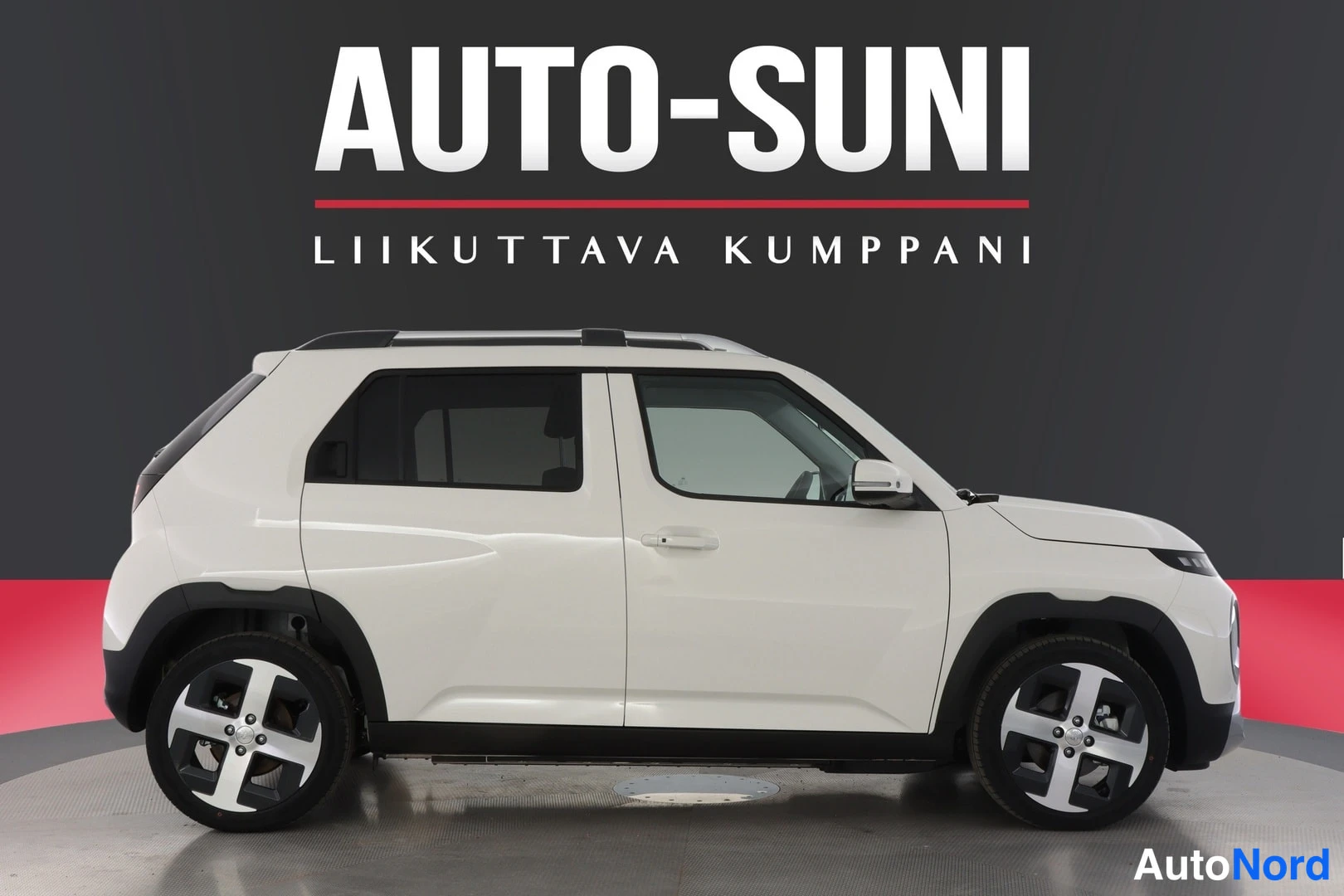 Sivulta: Valkoisen Hyundai Insterin sivuprofiili studiokuvassa; näkyvissä neljä ovea, tummat ikkunalasit ja kevytmetallivanteet.