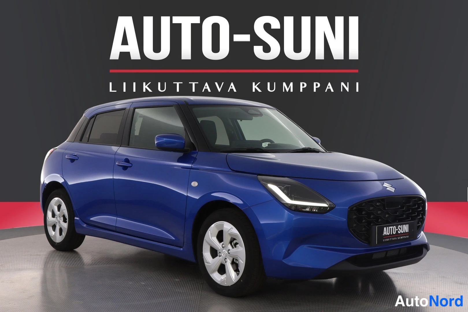 Etuviisto, nokka oikealle: Sininen Suzuki Swift -henkilöauto vinosti edestä kuvattuna studiochromaattisella taustalla.