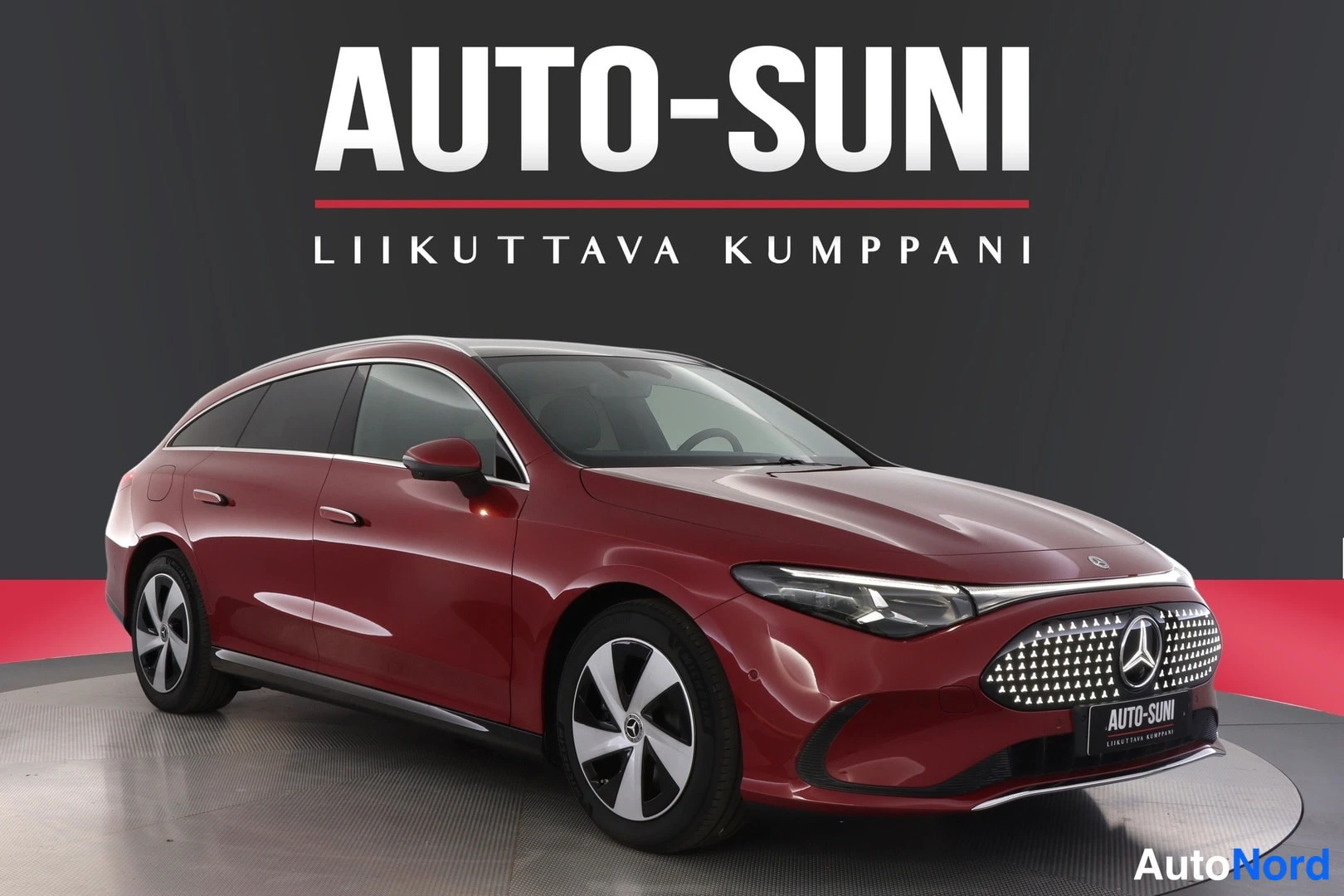 Etuviisto, nokka oikealle: Tummanpunainen Mercedes-Benz CLA -farmari etuviistöstä, keula kuvan oikeassa laidassa, studiotausta ja AUTOSUNI-banneri.