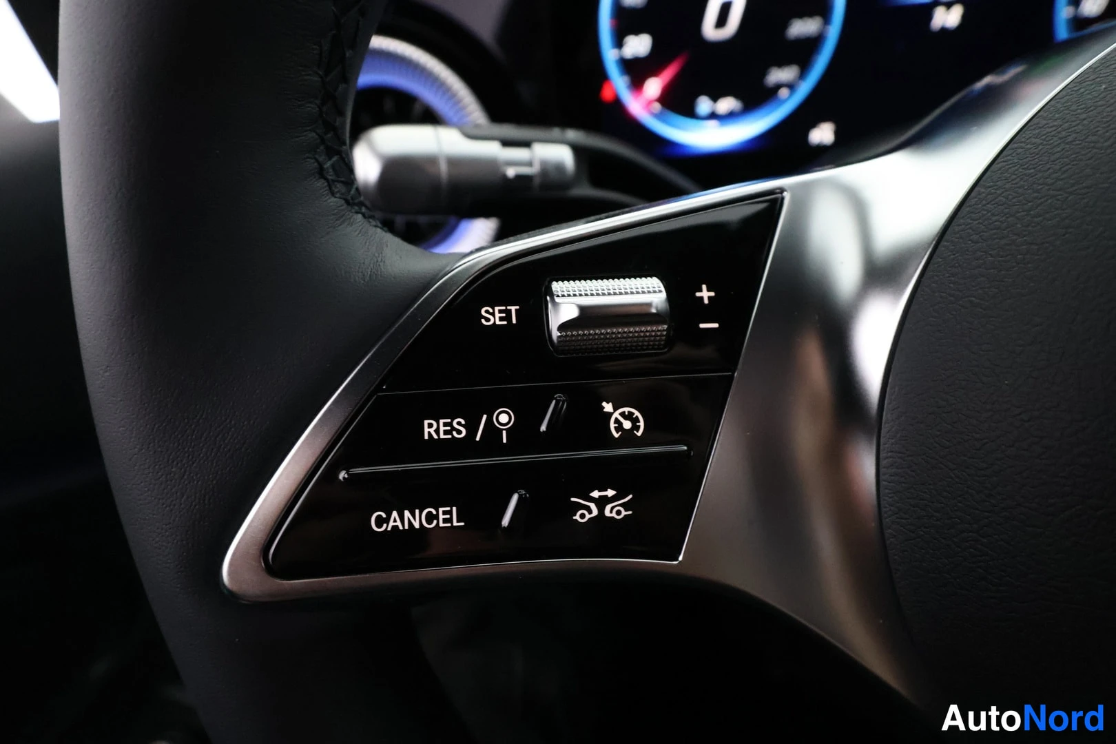 Yksityiskohta: Ohjauspyörän vasemman puolen cruise control -painikkeet merkinnöillä SET, RES ja CANCEL, taustalla digitaalinen mittaristo näytöllä 0.
