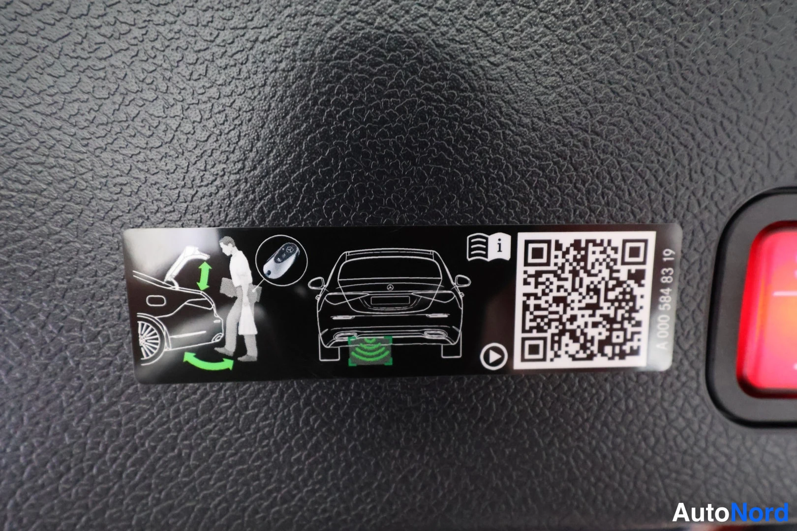 Yksityiskohta: Tarra porttikäskylaitteen käytöstä: autoa ja henkilöä esittävä kuvitus, QR-koodi ja numero A 000 584 83 19