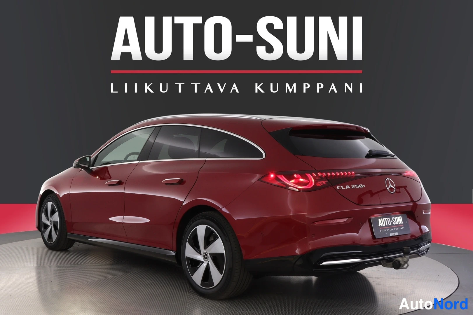 Takaviisto: Tummanpunainen Mercedes-Benz CLA -farmari takaaviistosta, perä kuvan oikeassa laidassa, takavalot palavat, takaovessa CLA 250+ -merkintä.