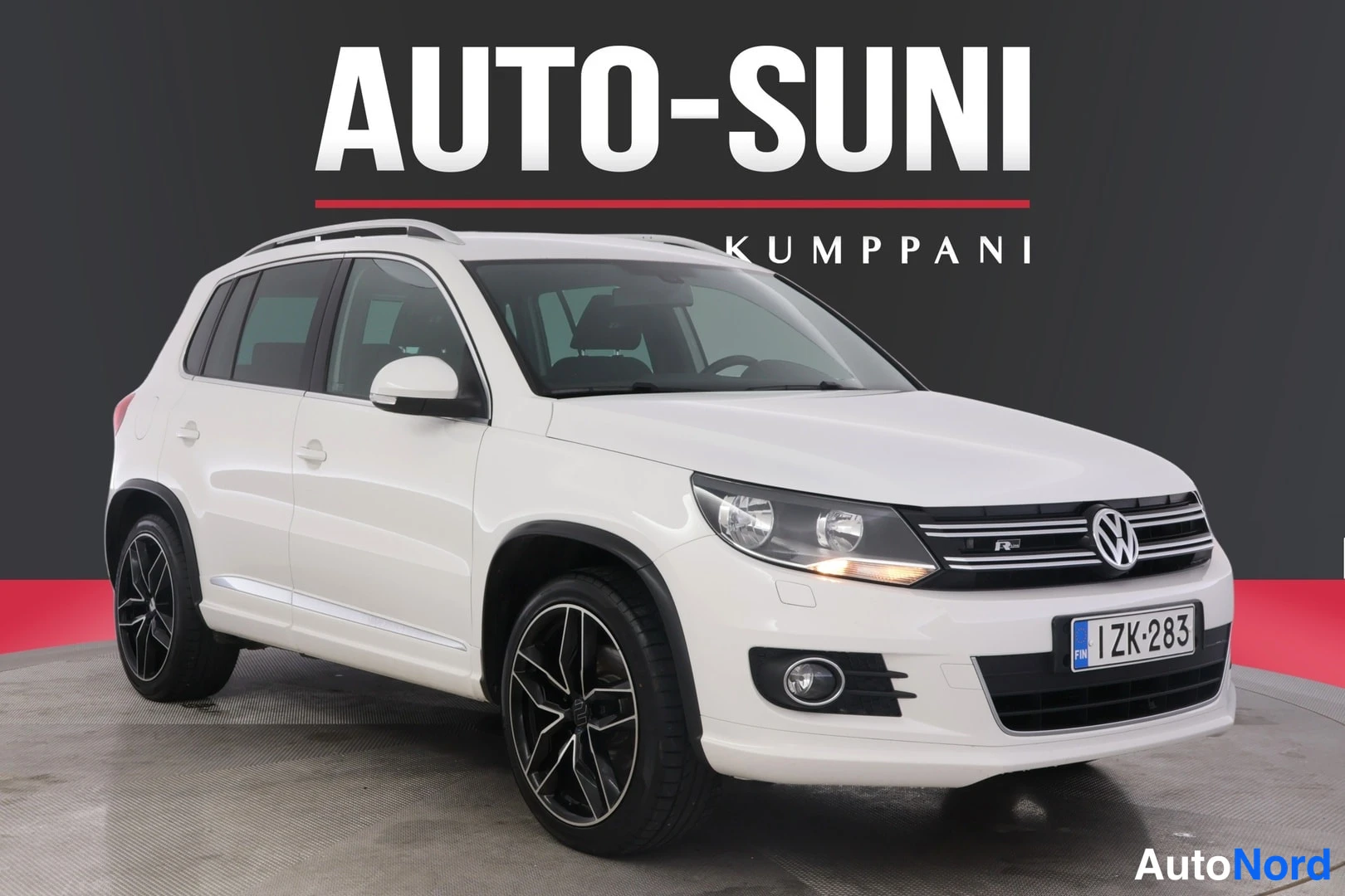 Etuviisto, nokka oikealle: Valkoinen Volkswagen Tiguan kulmassa edestä oikealta, rekisteritunnus näkyvissä etupuskurissa.