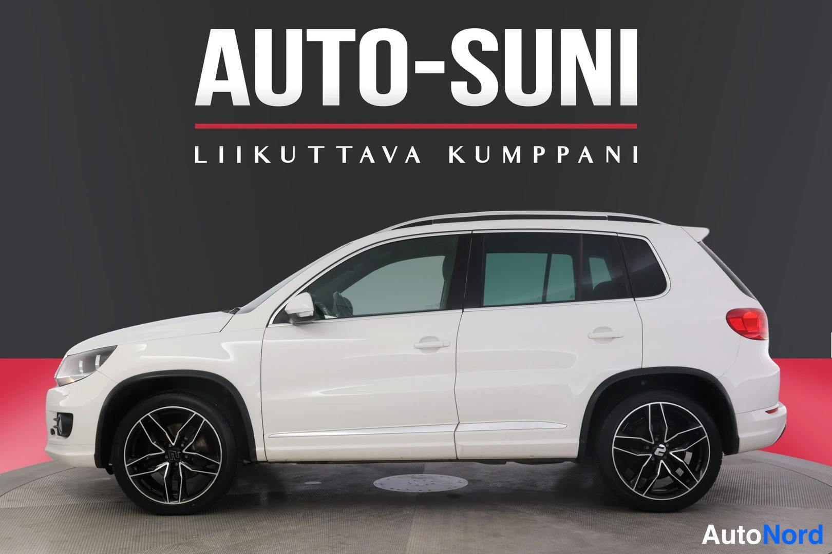Sivulta: Valkoinen Volkswagen Tiguan sivulta etukulmassa studio­taustaa vasten, AUTO-SUNI-logotietti kuvan yläosassa.