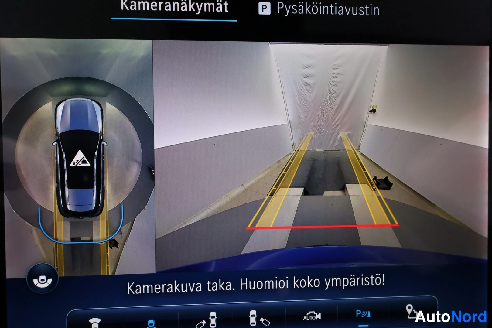 Muu: Mercedesin kameranäkymä näyttää ylhäältä- ja takakameran kuvan pysäköintiaukosta, otsikolla Kameranäkymät ja Pysäköintivakvustin.