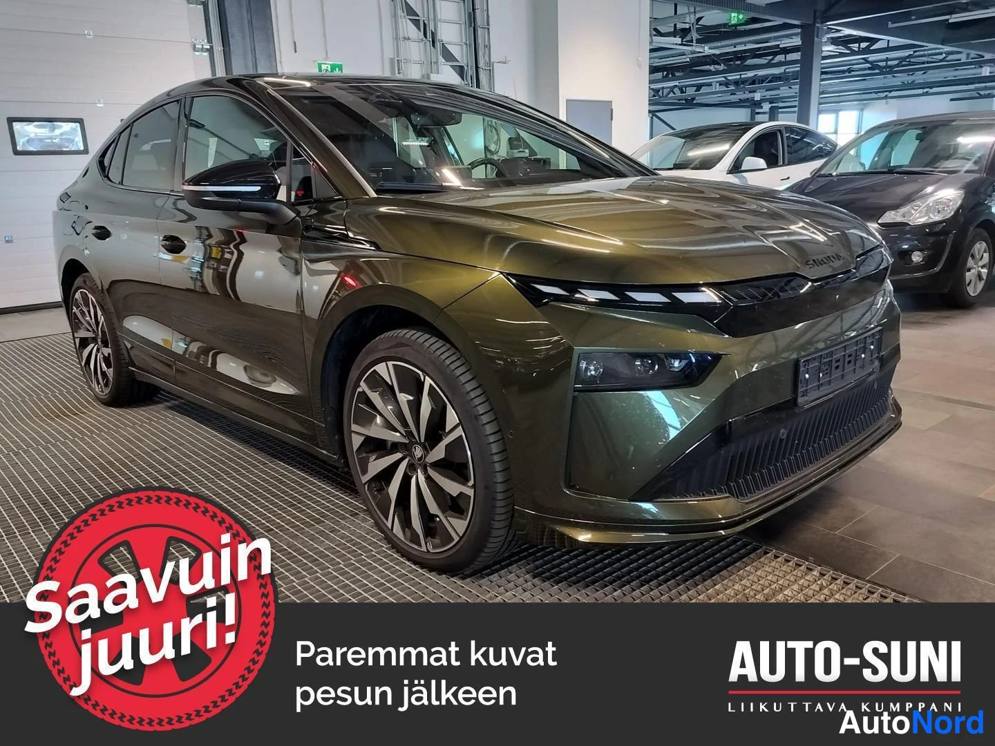 Etuviisto, nokka oikealle: Kulmakuva tummanvihreästä Skoda Enyaq Coupé -sähköautosta myymälätilassa, kohtisuora etunäkymä ja kylki näkyvissä.