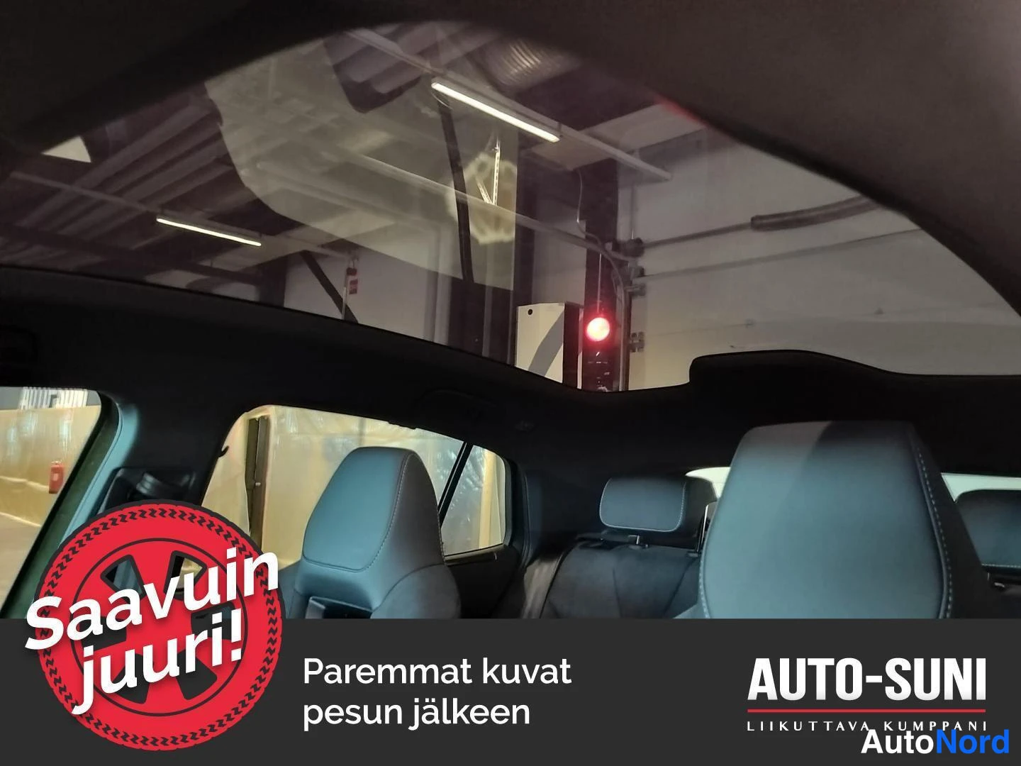 Muu: Näkymä auton sisältä ylöspäin laajalle lasikatolle, jonka läpi erottuu rakennuksen katto; kuvassa myös takaistuinten niskatuet.
