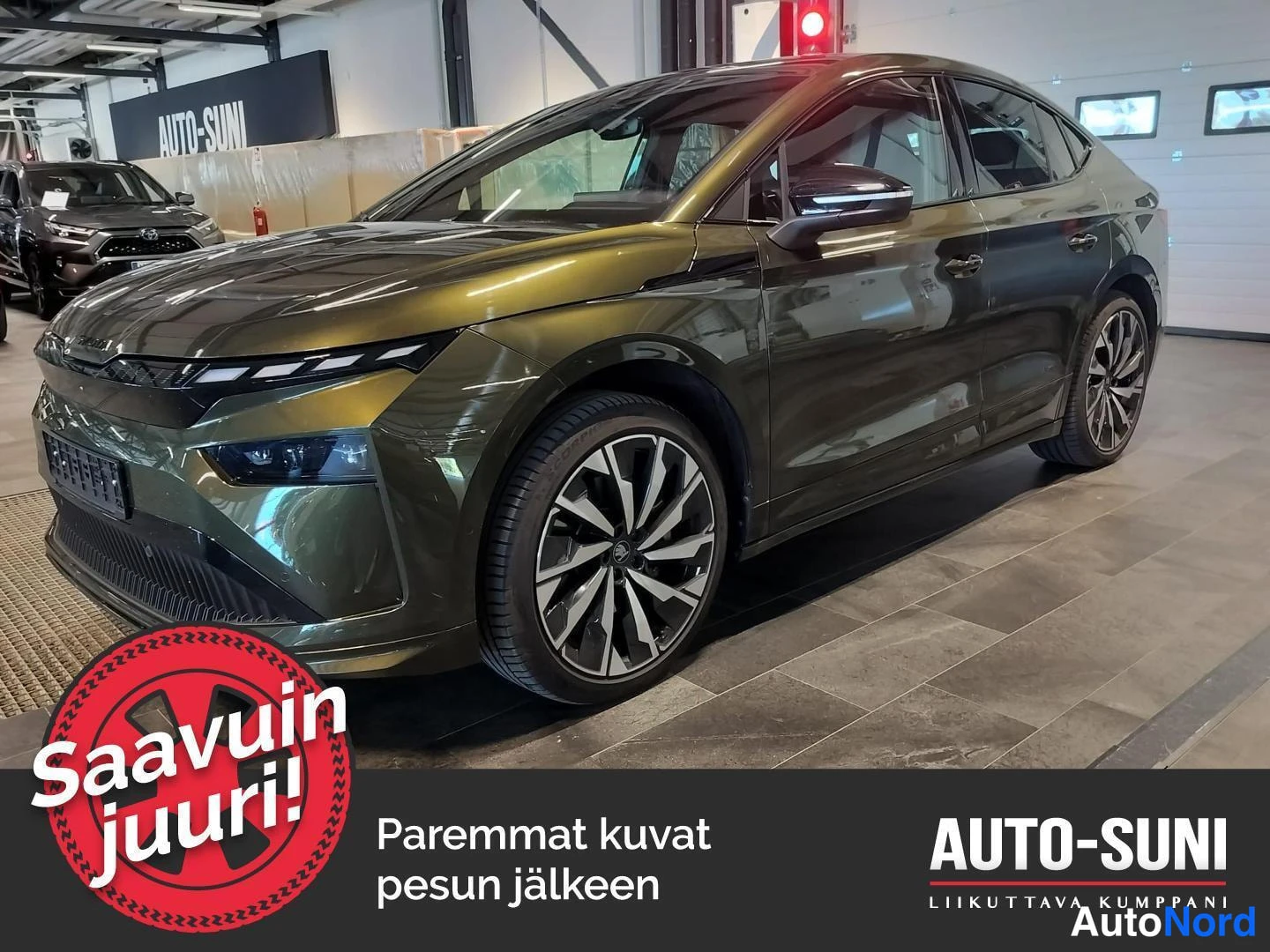 Etuviisto, nokka vasemmalle: Kulmakuva tummanvihreästä Skoda Enyaq Coupé -autosta autosalissa, keula vasemmalla ja kylki näkyvissä.