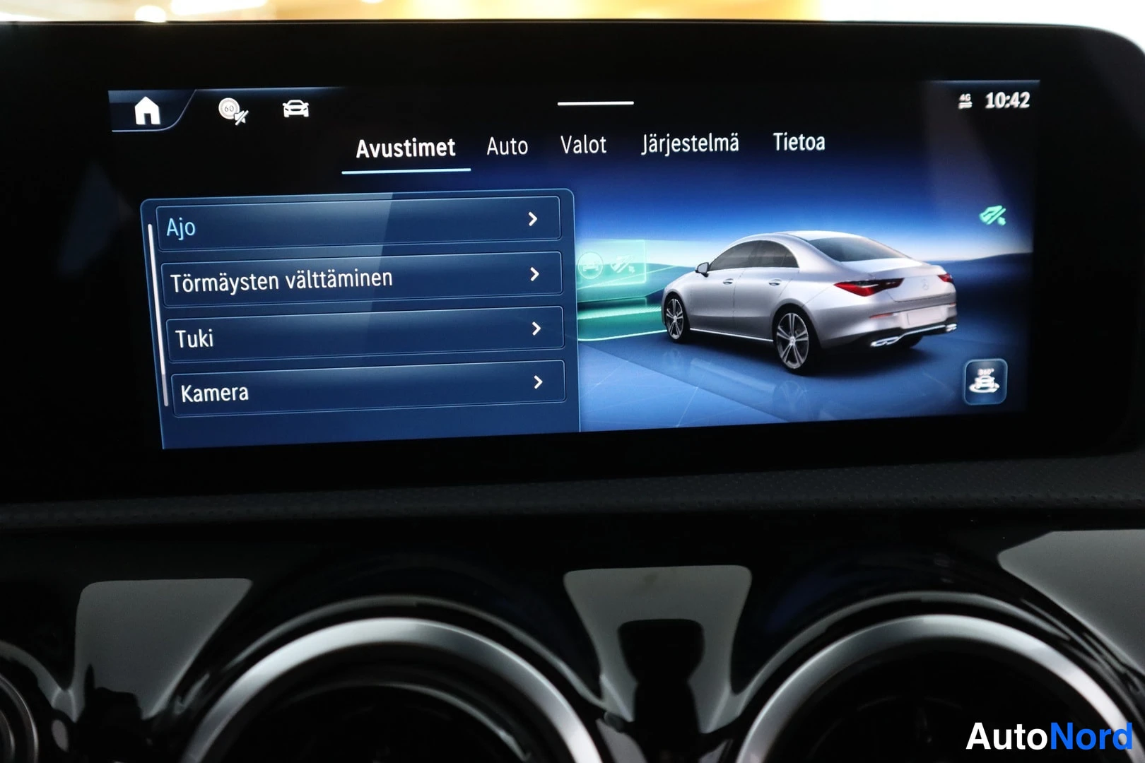 Muu: Keskimmäisen näytön Avustimet-valikko kohdilla Ajot, Törmäysten välttäminen, Tuki ja Kamera; ruudulla piirretty kuva hopeisesta autosta.