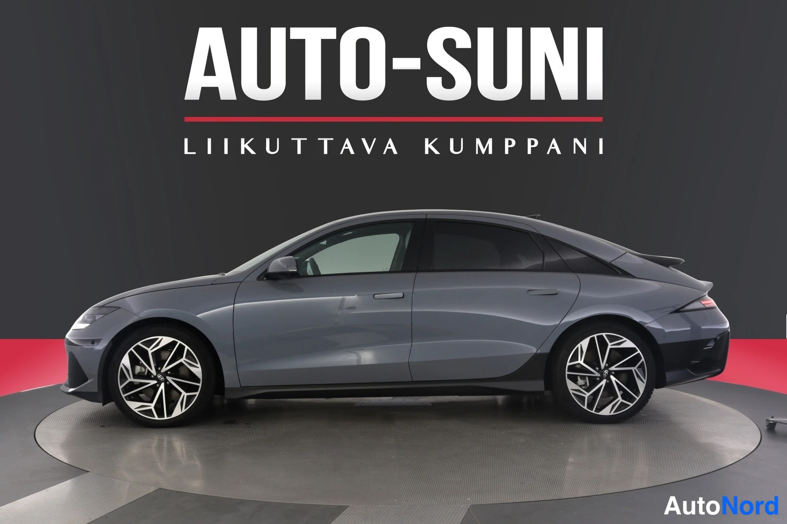 Sivulta: Hyundai IONIQ 6 -henkilöauton sivukuva, harmaansininen runko, valokuvassa Auto-Suni-mainosvaaka taustalla
